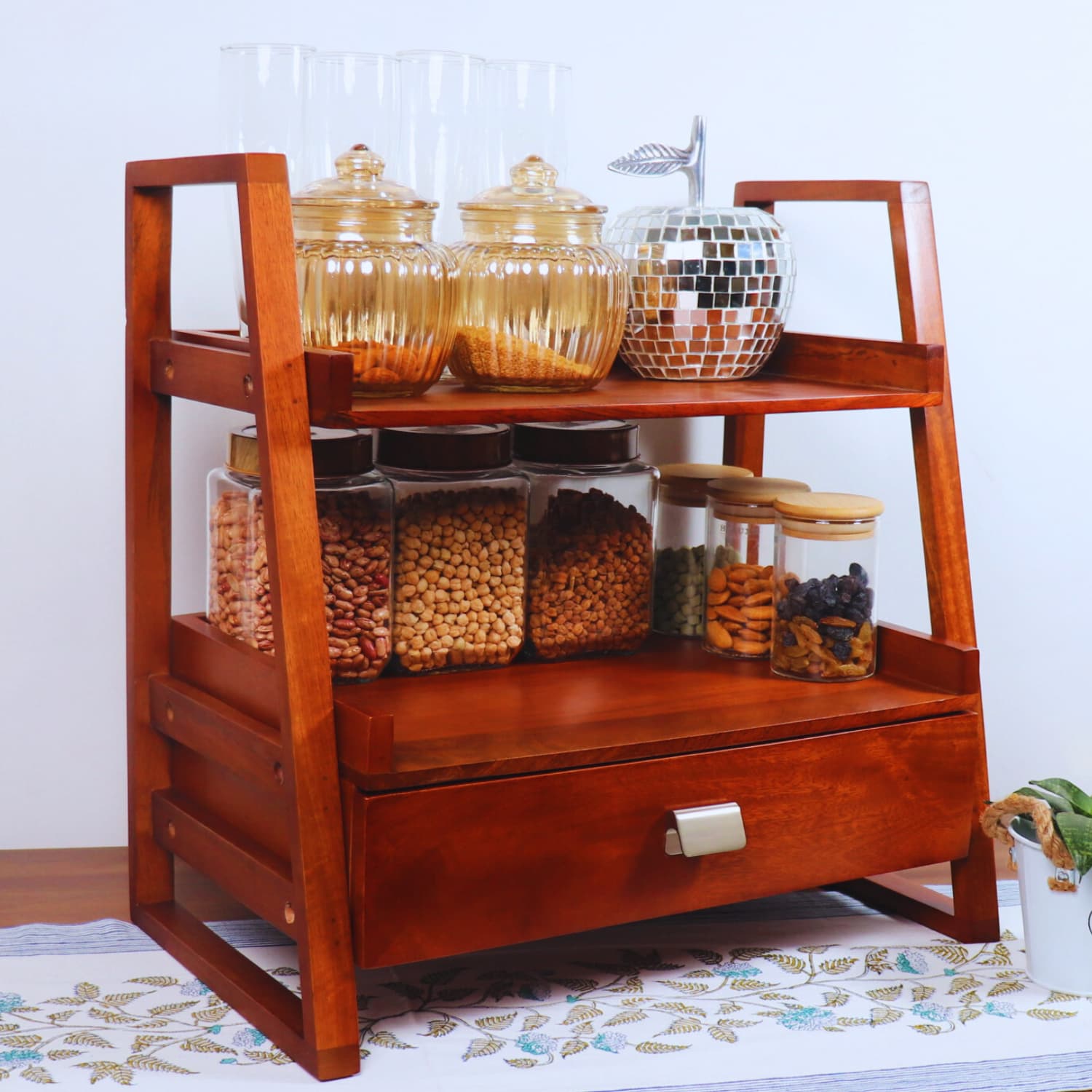 The LOOSEBUCKET Terra Manilla Wooden Kitchen Versatile Organizer with a vintage design features two shelves holding various jars filled with grains and legumes. The top shelf has glass jars, while the middle shelf contains jars with wooden and metal lids. Below is a drawer with a silver handle.