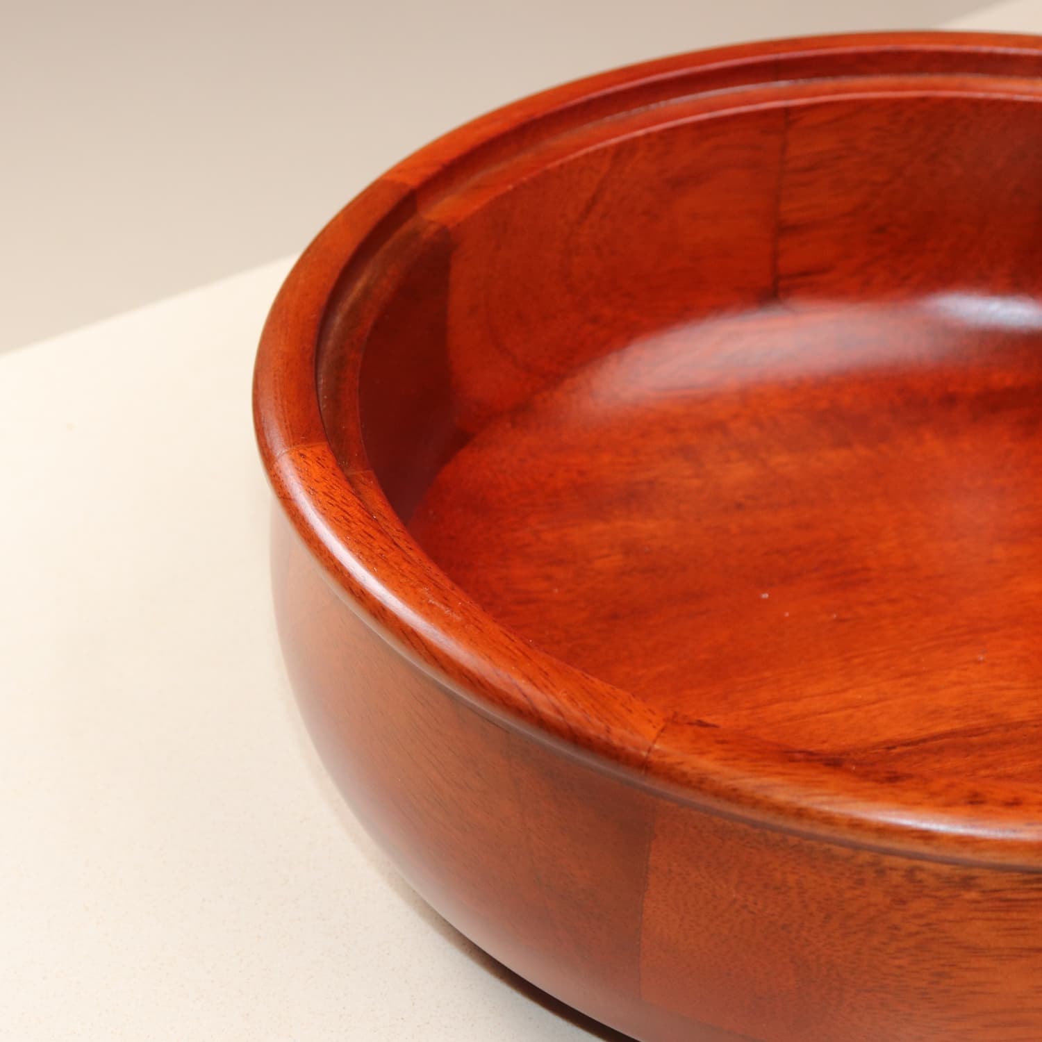 A close-up of a large, round, wooden bowl with a rich, polished finish. The bowl is empty and placed on a light-colored surface, showcasing its smooth texture and warm mahogany color. This could complement your kitchen as perfectly as The Woody Casserole Chapati box by LOOSEBUCKET online in India.